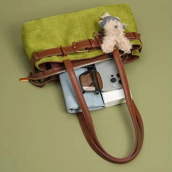 Green handbag with brown leather straps and a small plush toy on a green background