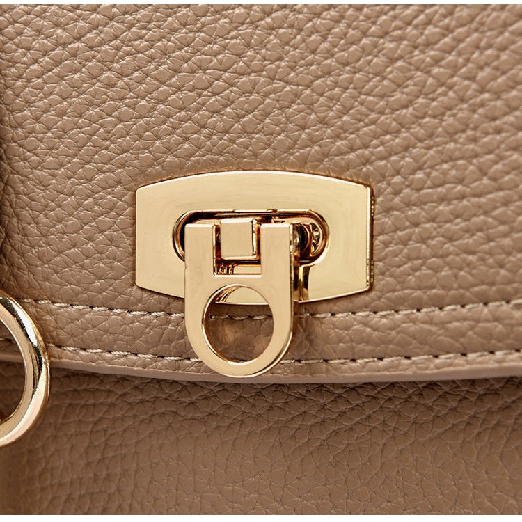 Close-up of a beige handbag with a gold clasp and tag.