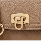 Close-up of a beige handbag with a gold clasp and tag.