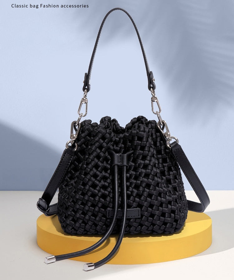 Black woven bucket bag on a yellow stand with a light blue background and text 'NEW.FASHION#' above.