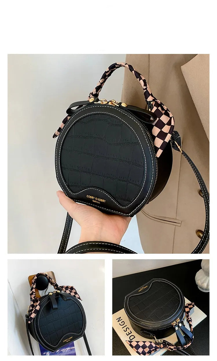 Black round handbag with checkered handle held by a hand, displayed against a neutral background.